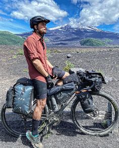 a man sitting on top of a motorcycle in the middle of an open field with mountains in the background