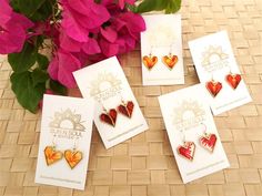 four heart shaped earrings sitting next to each other on top of a table with flowers in the background