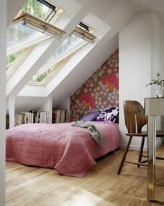 an attic bedroom with pink bedding and floral wallpaper, along with a chair