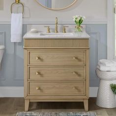 a white toilet sitting next to a bathroom sink under a round mirror above a wooden vanity