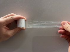 two hands are holding some clear tape on a gray surface, and one hand is pulling something out of the package