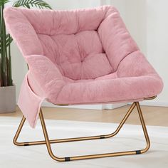 a pink chair sitting on top of a white floor next to a potted plant