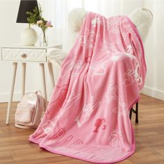 a pink blanket sitting on top of a wooden floor next to a white table and chair