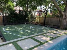 a backyard with a basketball court and swimming pool in the middle, surrounded by trees