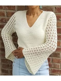 a woman standing in front of a brick wall wearing a white sweater and blue jeans