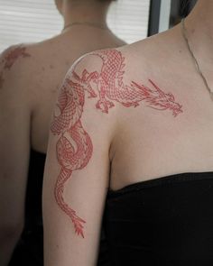 a woman with a dragon tattoo on her arm and shoulder is looking at herself in the mirror