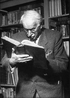 an old man reading a book in front of bookshelves