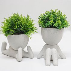 two cement planters sitting next to each other on top of a white surface with green plants in them