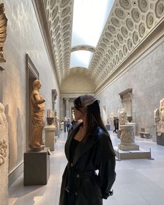 a woman standing in an art museum looking at statues and busturines on display