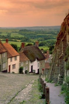 an old cobblestone street with houses on either side and green fields in the background