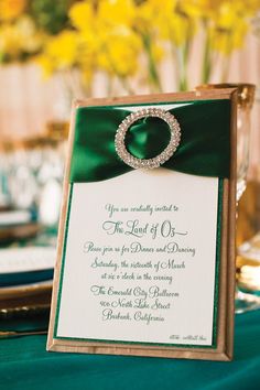 a green and white wedding card with a diamond ring on the front, sitting on top of a table