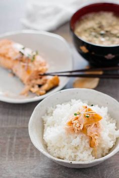 two white bowls filled with rice and some kind of meat on top of it next to chopsticks