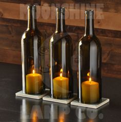 three wine bottles with candles in them on a table