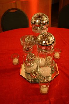 a table topped with lots of shiny dishes and disco ball centerpieces on top of a red cloth covered table