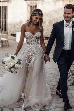 a bride and groom walking down the street holding hands in their wedding dresses with flowers on them