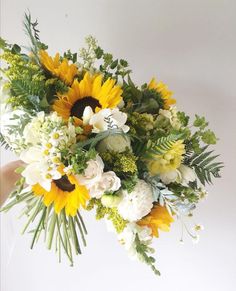 a bouquet of sunflowers and other flowers is held by someone's hand