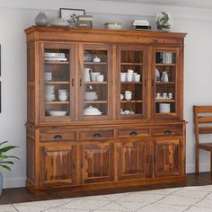 a wooden china cabinet with glass doors and drawers in a living room area next to a dining table