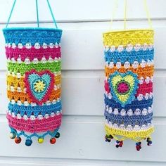 two colorful crocheted bags hanging from hooks on a wall with beaded bells