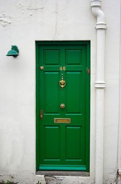 a green door is on the side of a white building with a light pole and lamp