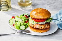 a chicken burger with lettuce, tomato and cucumber salad on a white plate