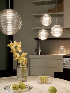 a white table topped with two vases filled with flowers and fruit next to hanging lights