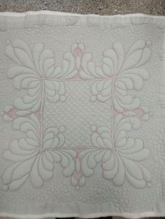 a white quilted table cloth with pink and white flowers on it, sitting on top of a stone floor