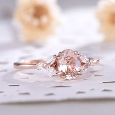 a pink diamond ring sitting on top of a white doily with flowers in the background