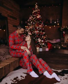 a man and woman in matching pajamas sitting next to a christmas tree