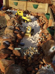 two children's toys are sitting in the sand on rocks and gravel next to a wooden fence