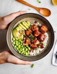 two hands holding a bowl filled with rice, peas and chicken on top of it