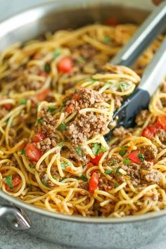 spaghetti with ground beef and tomatoes in a skillet being held by a spatula