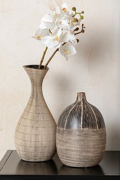 two vases with white flowers in them on a table next to a wallpapered background