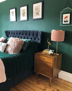 a bedroom with green walls and wooden flooring has a bed, nightstand, and two framed pictures on the wall