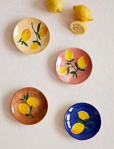 three plates with lemons painted on them next to two lemons and one slice of lemon