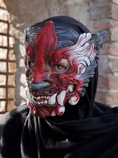 a person wearing a mask with red and white designs on it's face, standing in front of a brick wall