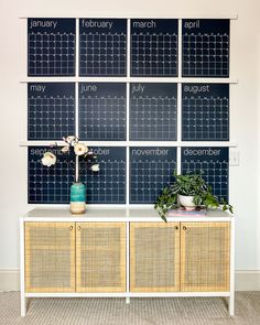 a calendar on a wall behind a cabinet with flowers in vases and potted plants