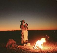 a man and woman standing next to a campfire