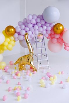 a gold giraffe statue surrounded by balloons and confetti on a ladder