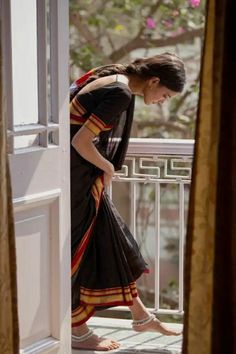 a woman in a black dress is standing on a balcony looking down at the ground