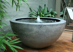 a concrete bowl with water coming out of it on a wooden table next to plants