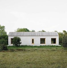 a white house sitting in the middle of a field with trees and bushes around it