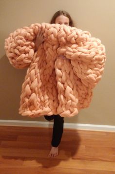 a woman standing in front of a wall holding up a giant chunky blanket