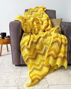 a yellow crocheted afghan is draped over a gray couch in a living room