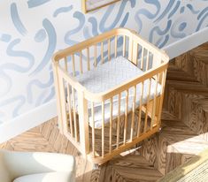 a baby crib sitting on top of a wooden floor next to a white chair