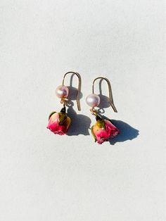 two pink flowers and pearls are hanging from gold earwires on a white surface