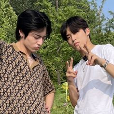 two young men standing next to each other in front of trees and grass, making the peace sign with their hands