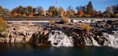 a waterfall in the middle of a river surrounded by rocks and trees with fall foliage