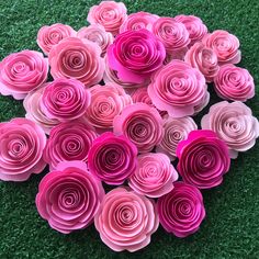 pink paper flowers arranged in the shape of a heart on green artificial grass, top view