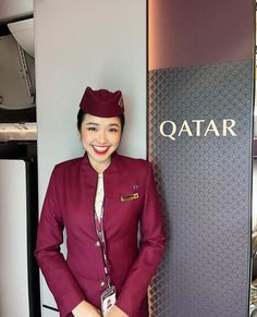 a woman standing next to a qatar sign in front of a wall with qantar written on it