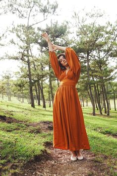 a woman in an orange dress is posing for the camera with her arms up and hands behind her head